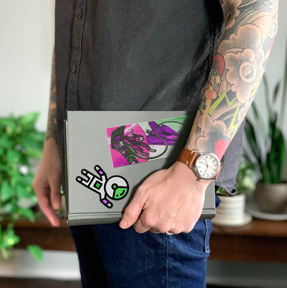 Man with tattoos holding grey notebook with holographic stickers on it